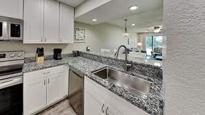 A modern kitchen with white cabinets, granite countertops, stainless steel appliances, and a built-in dishwasher. - Edgewater Villa #708 | Full-service resort! (Panama City Beach)