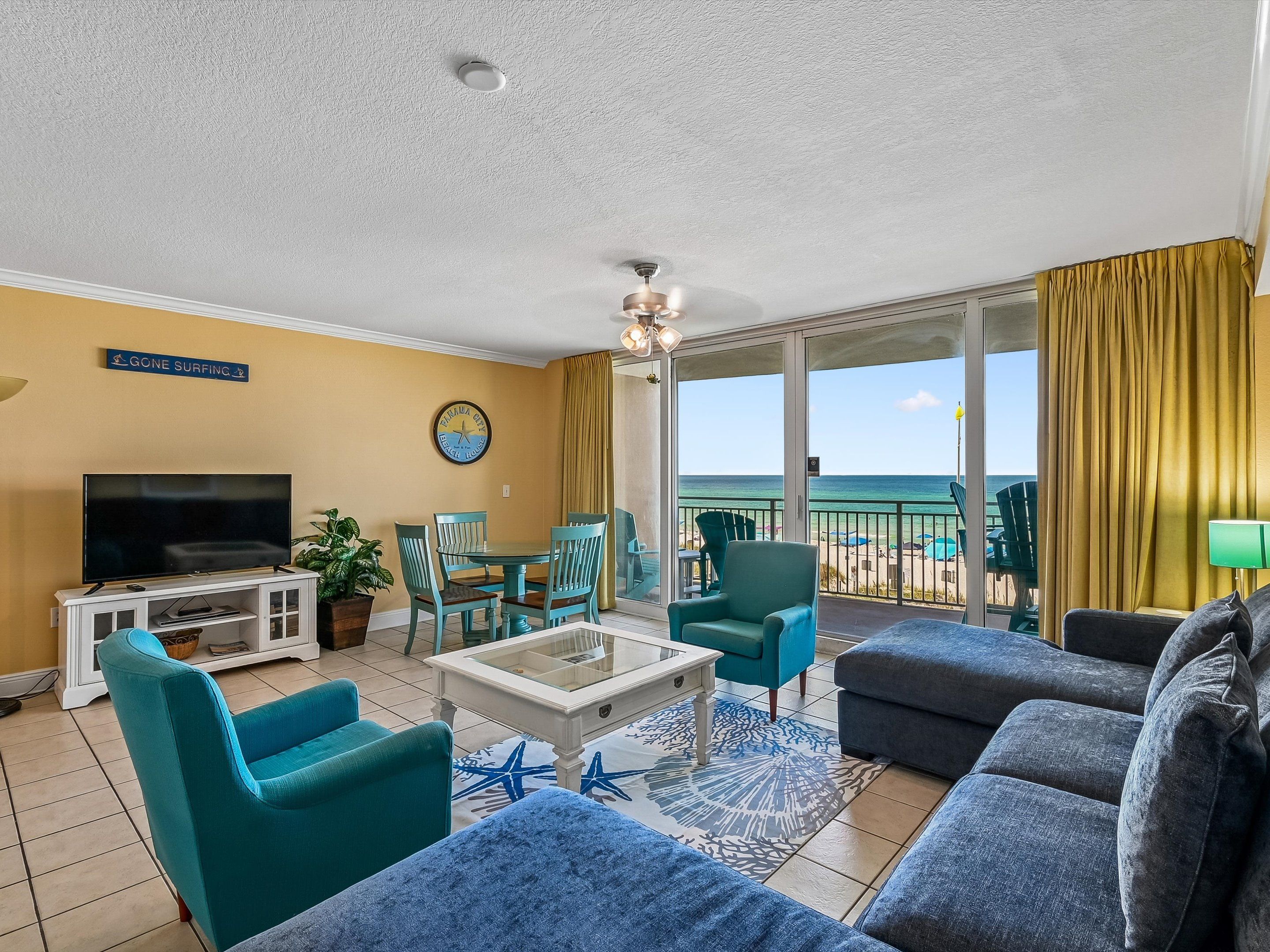 A room with a TV, seating, a clock, and a view of the beach.