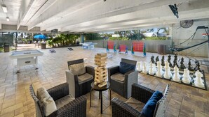 Un patio al aire libre con mobiliario de mimbre, una mesa de fútbol de mesa y un ajedrez grande.