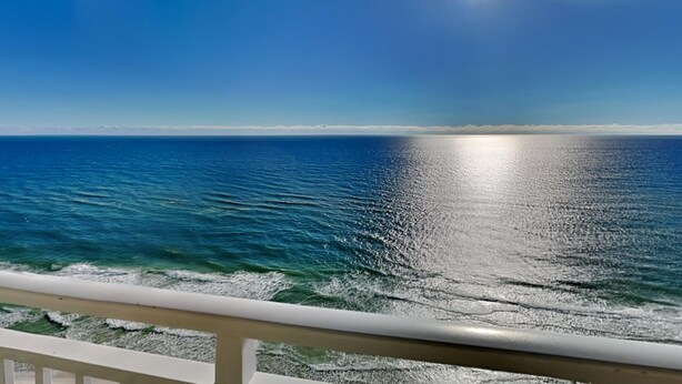 A clear view of the ocean with sunlight reflecting off the water, a distant shoreline, and a railing in the foreground. - Emerald Beach #2435 | Stunning Views + Resort Amenities! (Panama City Beach)