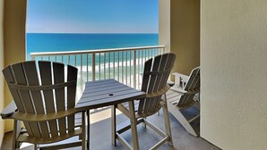 A balcony with two Adirondack chairs and a small table, overlooking a beach and the ocean. - Grand Panama Beach Resort - The Grand #1304 (Panama City Beach)