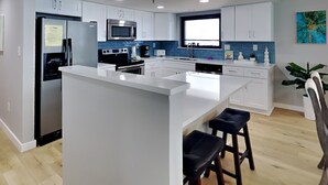 A modern kitchen with white cabinets, stainless steel appliances, and a central island with bar stools. - Watercrest #1401 | Warm turquoise waters! (Panama City Beach)