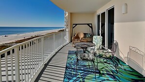 Uma varanda com vista para a praia, uma cadeira de balanço, uma mesa e uma cadeira.