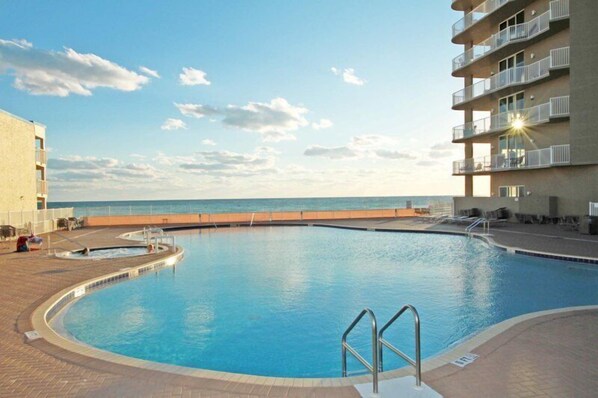 Piscina com vista para o oceano, rodeada por um edifício com varandas.