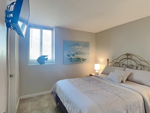 Un dormitorio con cama, ventana con persianas, un cuadro en la pared y una mesita de noche con lámpara.