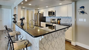 A modern kitchen with a central island, stainless steel appliances, and a patterned backsplash. - Long Beach I #503 | Balcony Views! (Panama City Beach)