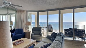 A spacious balcony with a view of the ocean, furnished with a sofa, chairs, and a table. - Long Beach I #506 | Luxe Condo, Spectacular Gulf Views + Amenities (Panama City Beach)