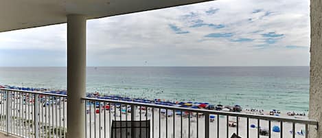 A balcony with a view of a crowded beach and the ocean.