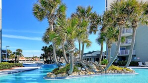 A swimming pool surrounded by palm trees and a building with balconies. - Long Beach I #800 | Beachfront + 3 Pools (Panama City Beach)