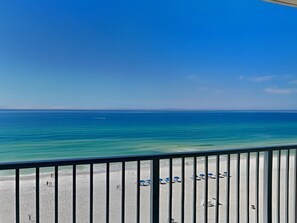 A beach view from a balcony with a railing, clear blue sky, and calm sea.