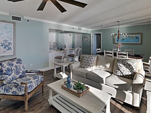 Een woonkamer met een bank, fauteuils en een salontafel. In de achtergrond bevindt zich een keuken.