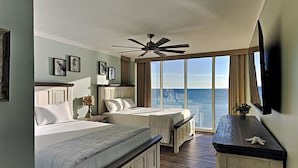 A hotel room with two beds, a ceiling fan, a large window with a view of the ocean, and a flat-screen TV mounted on the wall. - Long Beach I #900 | Updated Interior! (Panama City Beach)