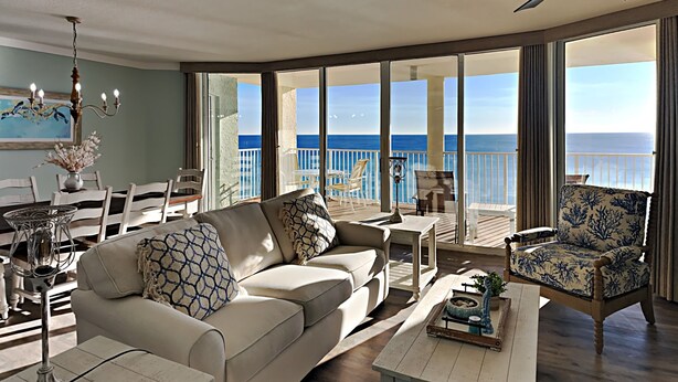 A spacious living room with a large window overlooking the ocean, a ceiling fan, and a dining area with a chandelier. - Long Beach I #900 | Updated Interior! (Panama City Beach)