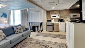 A compact living space with a kitchenette, a sofa with patterned cushions, a dining table, and a view of the outside. - Long Beach I #900E | Studio with Views! (Panama City Beach)