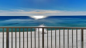 Blick auf einen Strand vom Balkon aus, mit Geländer, Meer und blauem Himmel.