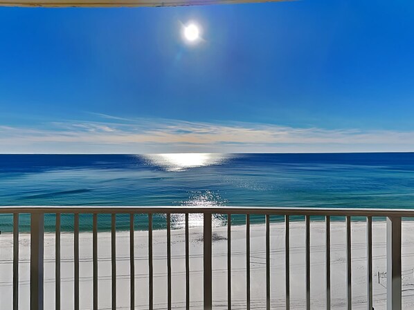 Vista a la playa desde un balcón con barandilla, océano y cielo despejado.