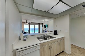 A modern kitchen with a dishwasher, double sink, and a view of the ocean through the window.