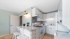 Eine moderne Küche mit weißen Schränken, einer Marmorarbeitsplatte und einem Einbauofen. Zwei weiße Hocker und ein Spülbecken mit Armatur sind vorhanden.