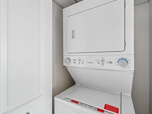 Vue de face d’une buanderie blanche, avec une machine à laver et un sèche-linge superposés.