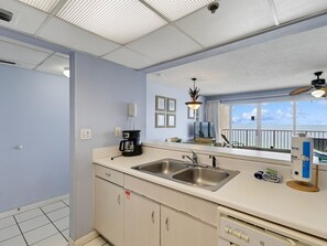 A kitchen with a double sink, a coffee maker, a telephone, and a window with a view of the sea.