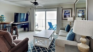 En moderne stue med ventilator, fladskærms-tv, spiseområde med en vase og en balkon med blå stole.