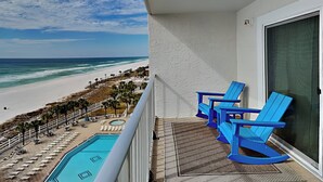En balkon med udsigt over stranden og havet, blå stole og en pool.