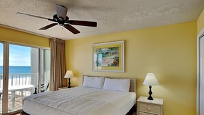 Een hotelkamer met een bed, twee bedlampen, een plafondventilator, een schilderij en een balkon met uitzicht op zee.