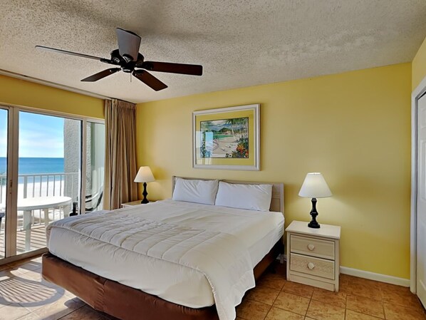 Een hotelkamer met een bed, twee bedlampen, een plafondventilator, een schilderij en een balkon met uitzicht op zee.