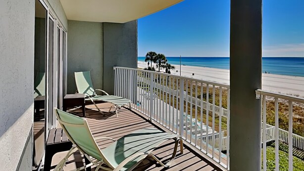 Een balkon met uitzicht op een strand, voorzien van een hekwerk en enkele stoelen.