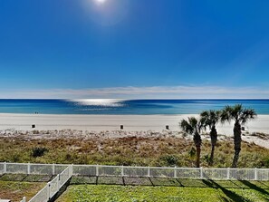 Blick auf einen Strand mit weißem Zaun, Palmen und blauem Himmel.