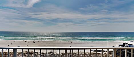 A beach view from a balcony with a railing, ocean, and distant shoreline.