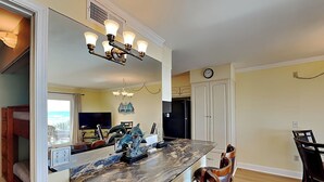 A kitchen with a marble countertop, wooden chairs, a clock on the wall, and a view of the ocean through a window. - Summit Beach Resort #429 | Gorgeous Views! (Panama City Beach)