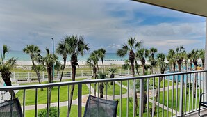 Een balkon met uitzicht op een strand, palmbomen en een omheind gebied met een zwembad.