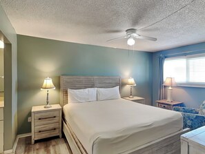 Ein Schlafzimmer mit einem Bett, zwei Nachttischen mit Lampen, einem Deckenventilator und einem Fenster mit Vorhängen.