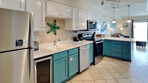 Una cocina moderna con armarios blancos, detalles en color verde azulado, una isla central, microondas y refrigerador.