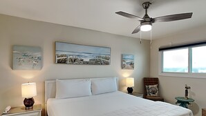 Een slaapkamer met een bed, twee nachtkastjes met lampen, een plafondventilator en kunstwerken aan de muren.