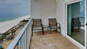 Een balkon met twee stoelen, uitzicht op het strand en een deur die leidt naar een kamer met een gestreept behang.