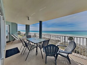 A balcony with a table and chairs, overlooking a beach.