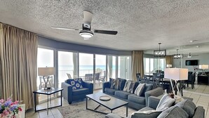 Ein großzügiger Wohnbereich mit Deckenventilator, einer Sofagarnitur, einem Couchtisch und Meerblick durch große Fenster.