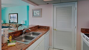 A kitchen with two stainless steel sinks, a countertop with a granite-like backsplash, white cabinets, and a door with louvered panels.