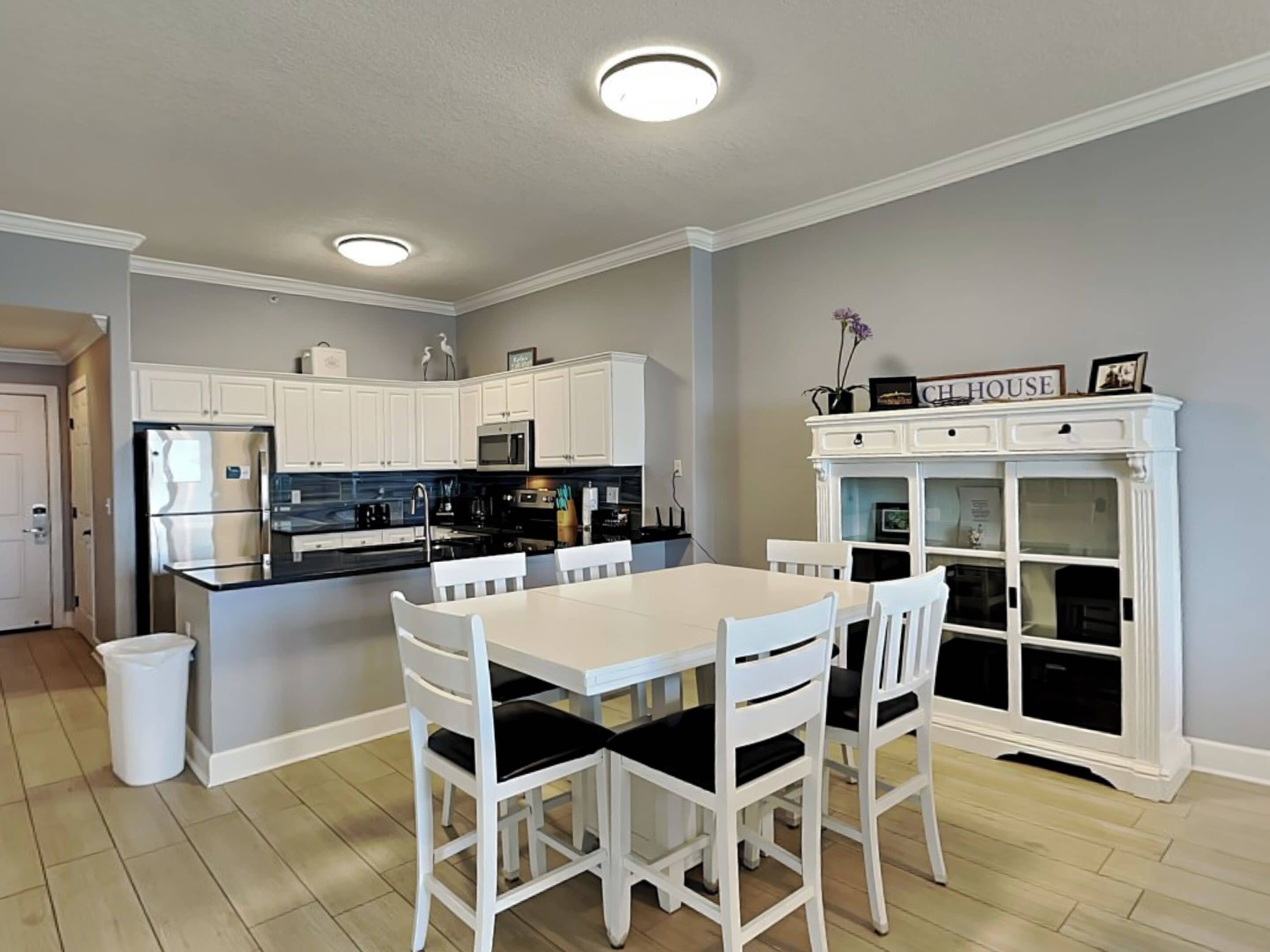 A modern kitchen with white cabinetry, a central island, and a dining area with white chairs.