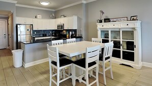Una cocina moderna con armarios blancos, una isla central y un comedor con sillas blancas.