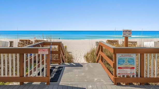A wooden boardwalk leading to a beach with a caution sign and a rip current warning sign. - Regency Towers #1202 | Gulf Front + Resort Amenities (Panama City Beach)