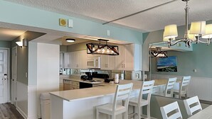 Une cuisine moderne avec des meubles blancs, un îlot central doté de tabourets et des luminaires suspendus.