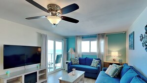 Una sala de estar con un televisor de pantalla plana, un sofá azul, una mesa de centro y un ventilador de techo.