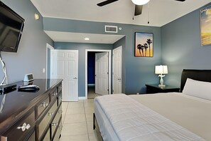 Un dormitorio con cama, cómoda, mesita de noche, lámpara, televisor y puertas que dan a otras habitaciones.