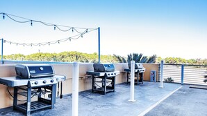 Une terrasse extérieure équipée de trois barbecues, de guirlandes lumineuses et offrant une vue sur un espace paysager aménagé.