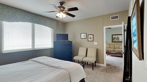 A bedroom with a bed, a ceiling fan, a dresser, two chairs, and a door leading to another room. - Shores of Panama #1111 | Pool + Gym! (Panama City Beach)