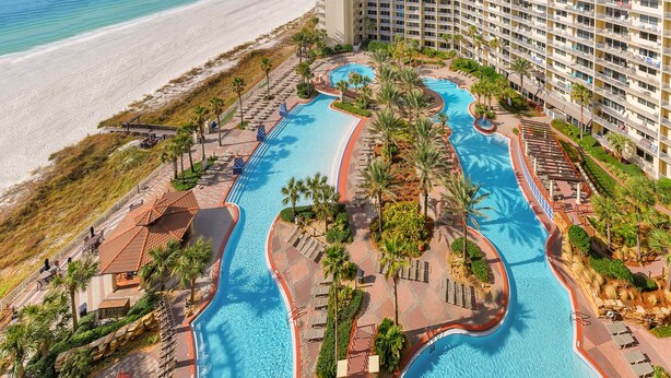 Un resort con un amplio área de piscina, una playa y un edificio de gran altura.