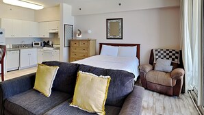 Ein Hotelzimmer mit Bett, Sofa, Sessel, Deckenventilator, Küchenzeile und einem Fenster mit Vorhängen.